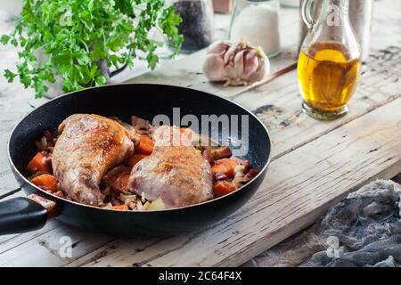 Fried rabbit legs on frying pan with vegetables and herbs Stock Photo