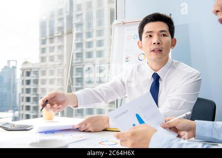 Portrait of serious busy young Asian businessman analyzing data in an office meeting with colleague in urban setting Stock Photo