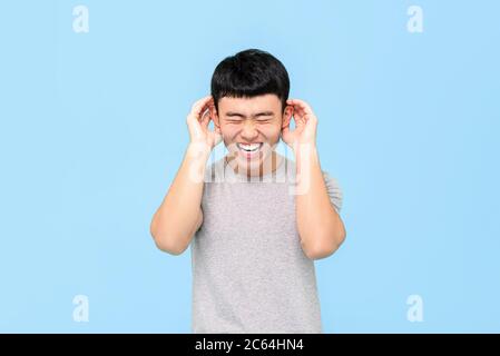 Funny portrait of laughing young Asian man holding his ears with both hands in isolated studio blue background Stock Photo