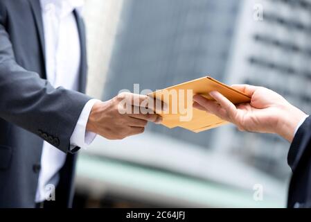 Close up portrait of  businessman hand recieving yellow envelope from boss in urban city background Stock Photo