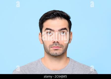 Close up portrait of serious handsome Caucasian man thinking while looking up in isolated studio blue background Stock Photo