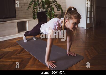 Young woman practicing pilates and yoga exercises at home. She is doing push-ups. Stock Photo