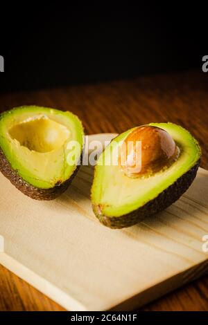 An avocado cut into half on a wooden cutting board with a dark background Stock Photo