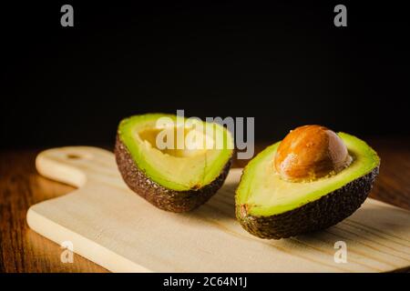 An avocado cut into half on a wooden cutting board with a dark background Stock Photo