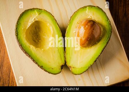 An avocado cut into half on a wooden cutting board with a dark background Stock Photo