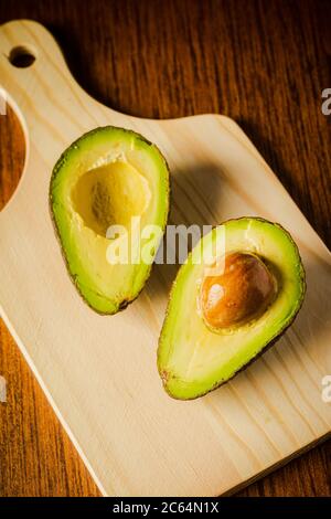 An avocado cut into half on a wooden cutting board with a dark background Stock Photo