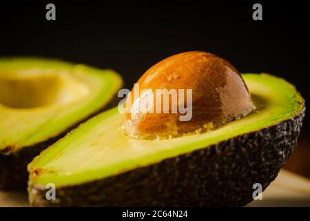 An avocado cut into half on a wooden cutting board with a dark background Stock Photo