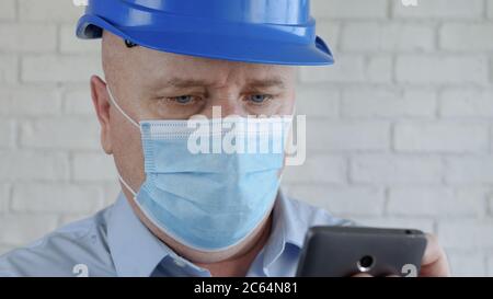 Engineer with Safety Helmet and a Protection Mask on His Face Talking to the Cell Phone Stock Photo