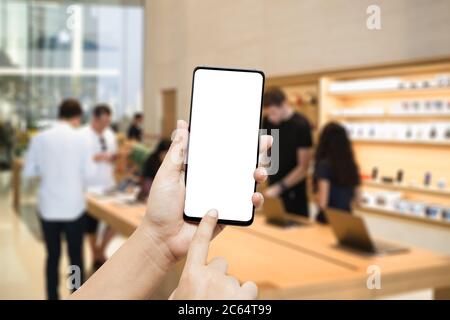Mockup smartphone hand holding the black smartphone with blank white screen and modern frame less design in the modern computer, IT and Gadget store b Stock Photo