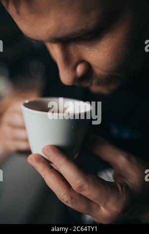 Barista inhales the aroma of fresh espresso from a white cup - a professional assessment of the quality of coffee Stock Photo