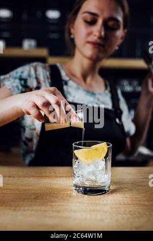 Girl bartender adds syrup to a glass with ice and lemon while making a cocktail - female drink Stock Photo