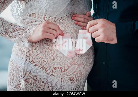 man and woman are holding in their hands small baby socks on a pregnant belly Stock Photo