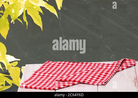 Closeup of a empty red checkered tablecloth or napkin on a rustic bright table against black wall with yellow maple. Template for food and product dis Stock Photo
