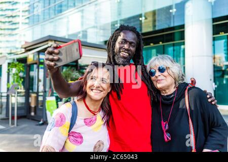 Black man with dreadlocks and two Caucasian women taking selfie with mobile phone. Stock Photo