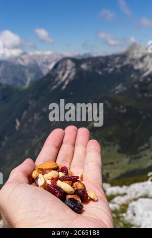 Hand holding a healthy snack on the top of the mountain. Consisting of different nuts and dried fruit, with beautiful background of mountains. Stock Photo