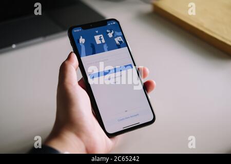 CHIANG MAI ,THAILAND - JULY 3, 2020 : Woman hand holding iPhone X to use facebook with login screen.Facebook is a largest social network and most Stock Photo