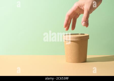 Craft paper soup cup and female hand on brown background. Ecological individual package. Zero Waste. Stock Photo