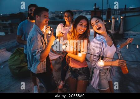 Friends enjoying cocktails at a party. Group of happy people having fun, dancing on a rooftop Stock Photo