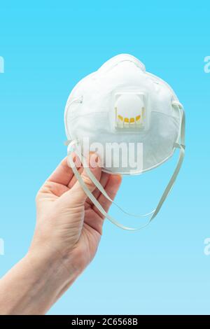Hand with the respiratory protection face mask on blue background Stock Photo