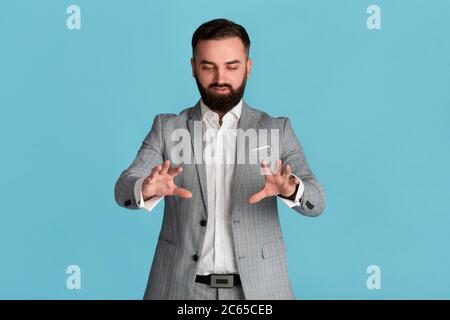 Serious young entrepreneur touching interactive virtual screen on blue background, space for design Stock Photo
