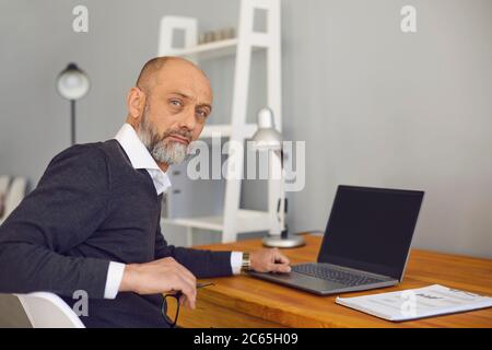 Online job concept. Serious elderly man working or studying at home on his laptop computer, mockup for design Stock Photo
