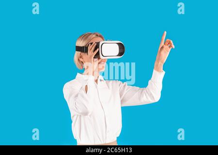Business lady wearing VR headset and pointing finger at imaginary screen on blue background Stock Photo