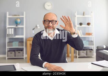Waving old businessman smiling looking at the camera video call web camera gadget sitting in the apartment. Stock Photo
