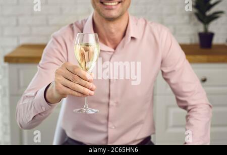 A glass of champagne in a man's hand. A young man holds a glass of wine looking at the camera on a laptop video conference monitor. Stock Photo