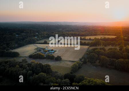 Aerial shot of farmland and house surrounded by woodland in Surrey, UK. Sunset Stock Photo
