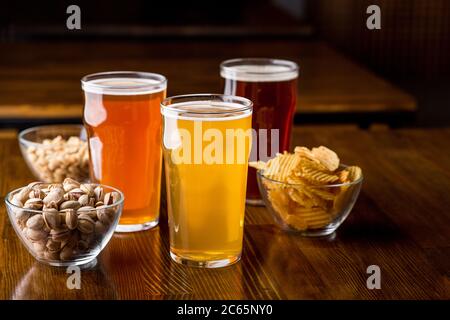 Different drinks in glasses. Pistachios, chips, peanuts in glass in plates on wooden table Stock Photo