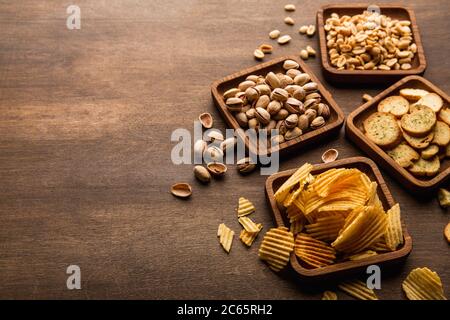 Crispy snacks. Rusks, peanuts pistachios and chips in square wooden plates on brown table Stock Photo