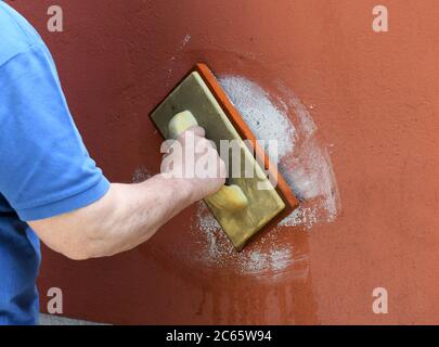 Bricklayer grouting masonry on a colored wall in a close up on his hand as he applies the grout in a maintenance, construction or renovation concept Stock Photo