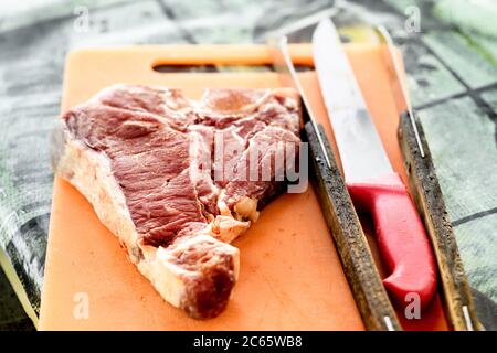 Raw Florentine beef steak on a cutting board with kitchen knives ready for cooking in a high angle close up view Stock Photo