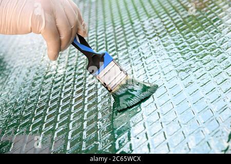 Person refreshing the green paint on a metal grid with diamond pattern in a close up view of a gloved hand and paintbrush Stock Photo