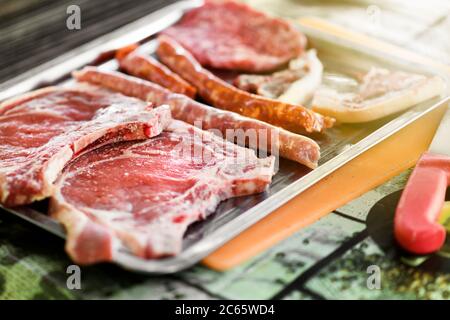 Tray with assorted raw rib eye steaks and spicy sausage ready to barbecue in a close up view Stock Photo