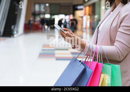 Cashback Bonus. Woman With Shopper Bags Using Smartphone In Mall After Shopping Stock Photo