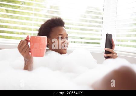 Woman with coffee cup using smartphone in a bathtub Stock Photo