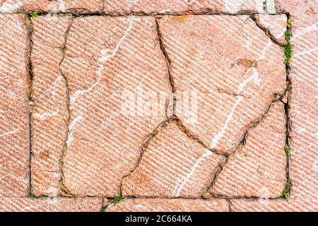 Cracks on the road red tile. Sprouted green grass in the crack. Copyspace. Abstract background. Old road surface Stock Photo