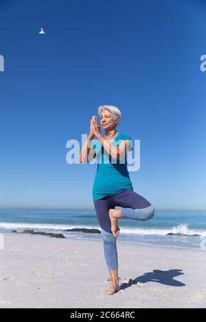 Senior Caucasian woman sitting on sand and practicing yoga Stock Photo
