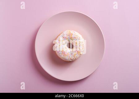 Vanilla donut with sprinkles on pink plate, sweet glazed dessert food on pink minimal background, top view Stock Photo