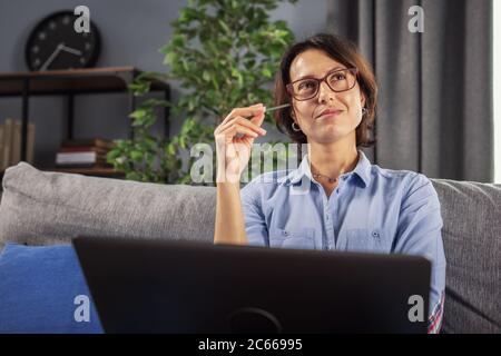 Lady sitting on sofa with laptop and looking for inspiration Stock Photo
