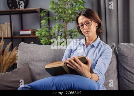 Beautiful lady relaxing on cozy sofa with interesting book Stock Photo