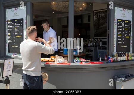 With the Coronavirus pandemic lockdown rules being eased, pubs have now re-opened and a staff member wearing a face shield serves a customer from an outdoor street counter in Greenwich, on 5th July 2020, in London, England. Stock Photo