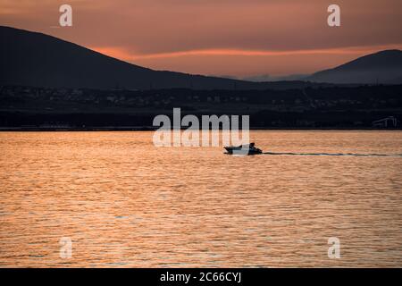 the coast and bright orange summer seascape at sunset, a pleasure yacht against the backdrop of the mountains of the resort city of Gelendzhik Stock Photo