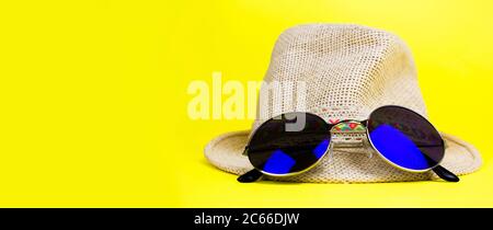 Womens summer straw hat with a brim, blue rounded sunglasses on yellow background side view copy space. Banner. Stock Photo