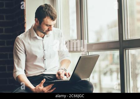 handsome man hold a laptop in his hands near the window. He works on an important task at home Stock Photo