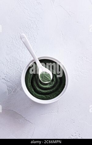 Spiral made of green chlorella or spirulina powder in white porcelain bowl from above and spoon on top of it. Healthy superfood eating and dieting con Stock Photo