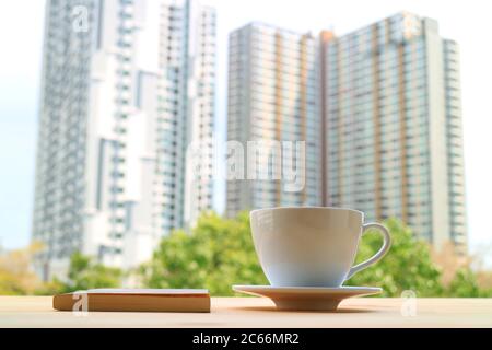 Cup of coffee with a book against blurry modern high buildings in the backdrop Stock Photo