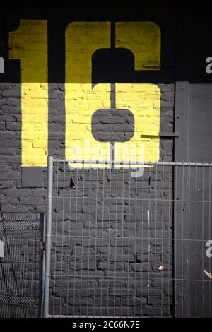 A large yellow building number painted on a striking dark gray painted brick wall, Stock Photo