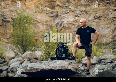 a tourist dressed in sportswear is leaning with his right leg on the stone on the background of rocks. A traveler poses for a photo shoot in memory of Stock Photo